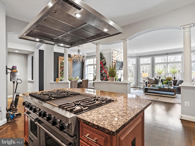 kitchen featuring island exhaust hood, a wealth of natural light, an inviting chandelier, range with two ovens, and dark stone countertops