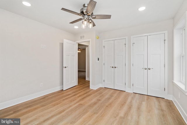 unfurnished bedroom with light hardwood / wood-style flooring, ceiling fan, and multiple closets