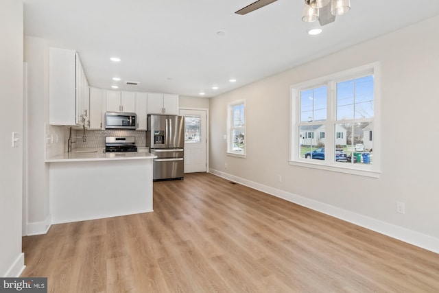 kitchen with ceiling fan, stainless steel appliances, tasteful backsplash, white cabinets, and light wood-type flooring