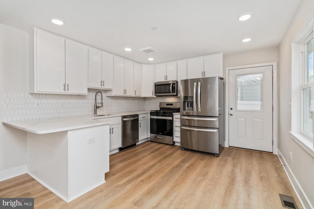 kitchen with sink, stainless steel appliances, backsplash, white cabinets, and light wood-type flooring