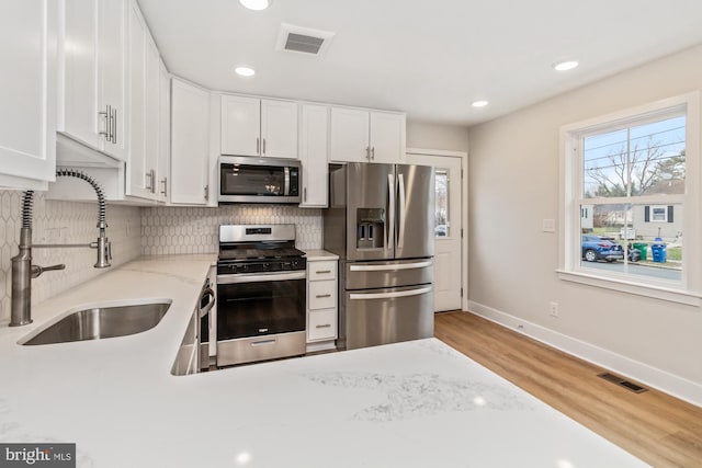 kitchen with stainless steel appliances, white cabinetry, light hardwood / wood-style floors, and sink