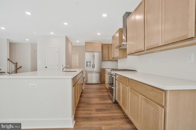 kitchen with recessed lighting, wood finished floors, a sink, appliances with stainless steel finishes, and wall chimney exhaust hood