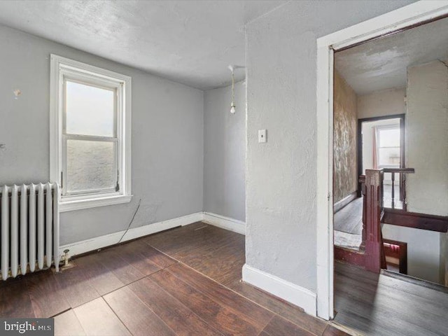 unfurnished room featuring radiator heating unit and dark hardwood / wood-style floors