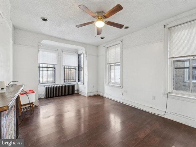 unfurnished living room featuring ceiling fan, radiator heating unit, dark wood-type flooring, and a textured ceiling