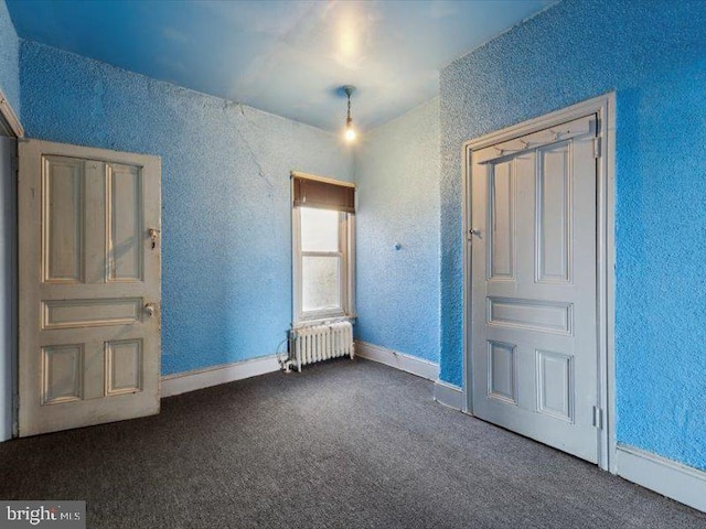 unfurnished bedroom with dark colored carpet and radiator heating unit