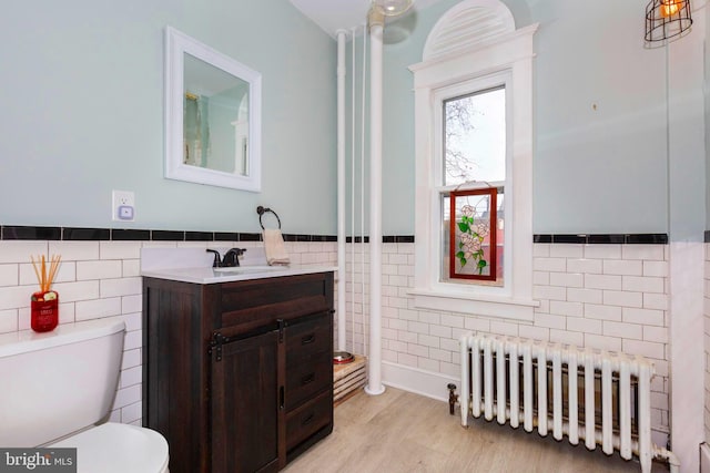 bathroom with vanity, hardwood / wood-style floors, tile walls, radiator heating unit, and toilet