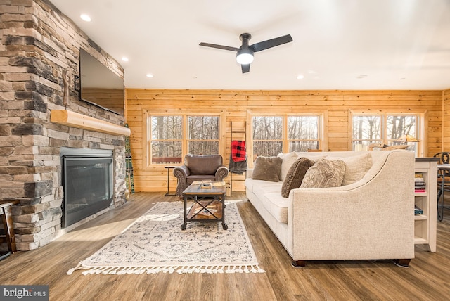 living room with ceiling fan, wood walls, wood-type flooring, and a fireplace