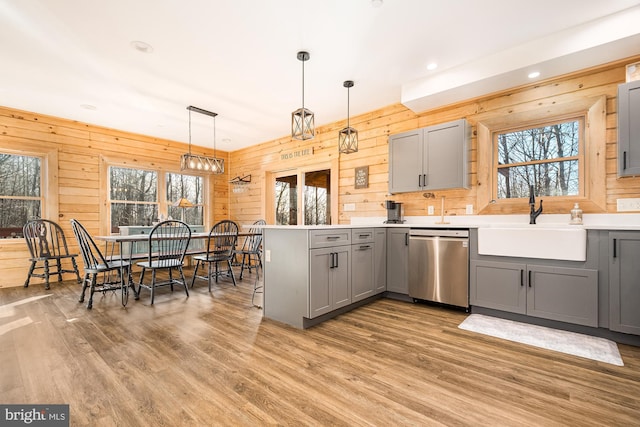 kitchen with stainless steel dishwasher, light hardwood / wood-style floors, sink, pendant lighting, and gray cabinets