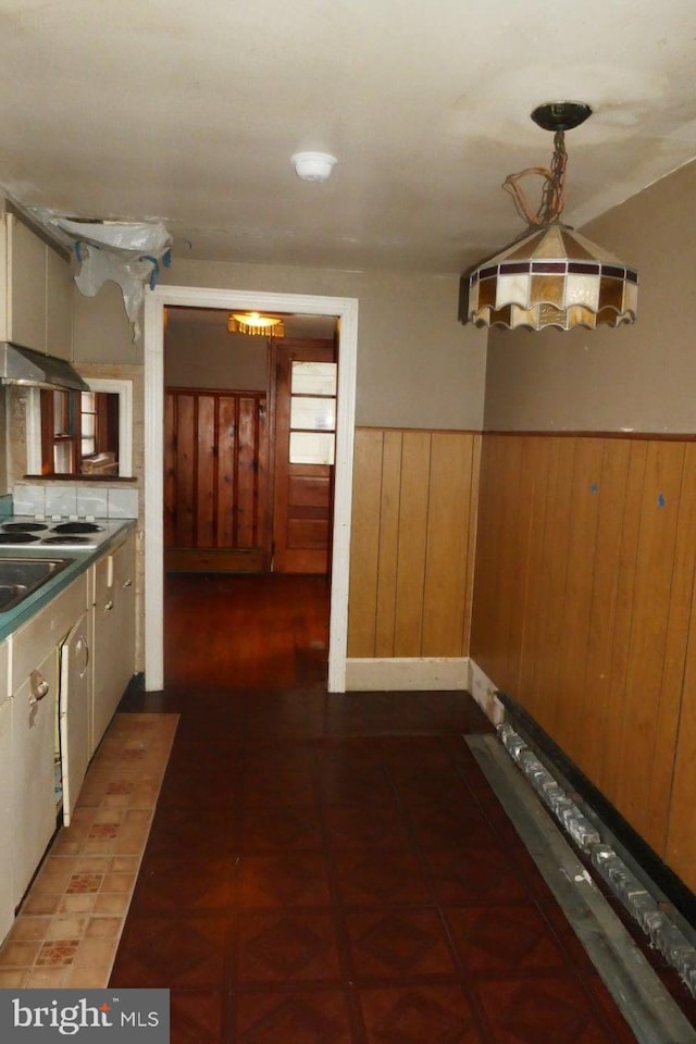 kitchen with backsplash, wooden walls, stainless steel stovetop, and hanging light fixtures