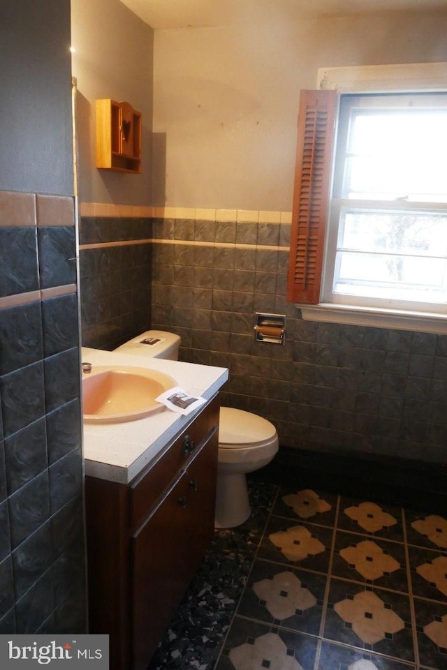 bathroom with tile patterned flooring, vanity, toilet, and tile walls