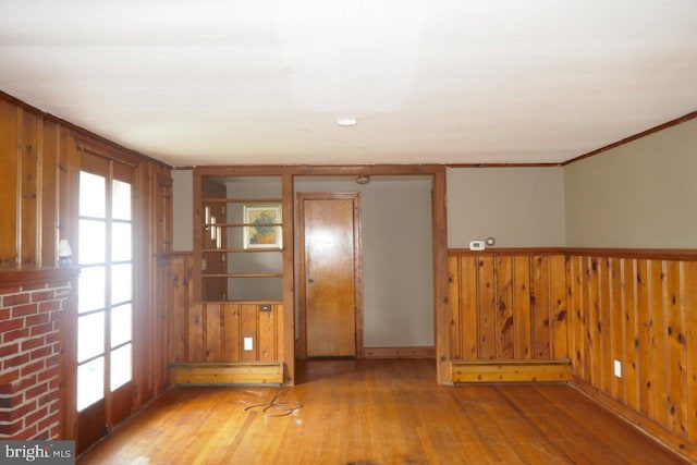 empty room featuring hardwood / wood-style flooring, wood walls, and baseboard heating