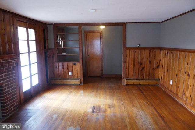 unfurnished living room featuring light wood-type flooring, a baseboard radiator, a healthy amount of sunlight, and wood walls