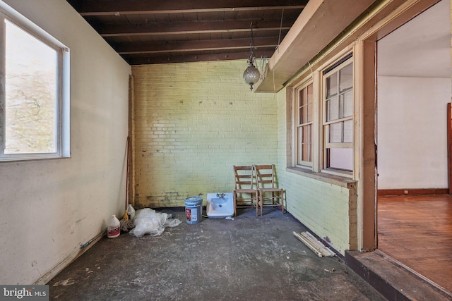 interior space featuring beam ceiling, a wealth of natural light, and brick wall