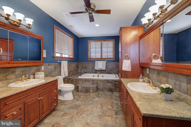 bathroom featuring vanity, toilet, a relaxing tiled tub, and ceiling fan