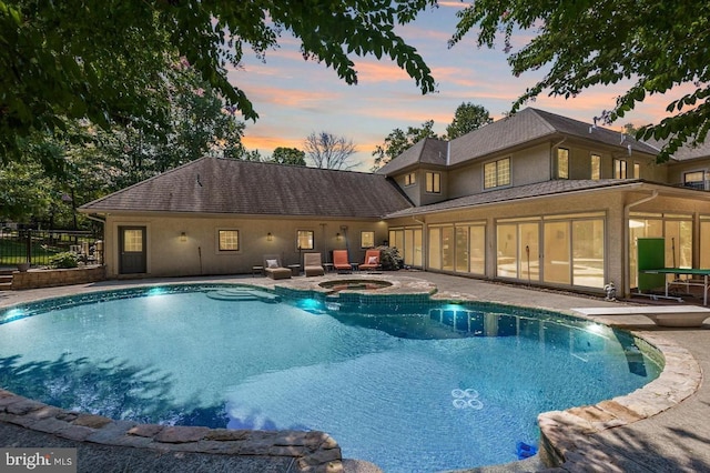 pool at dusk with an in ground hot tub and a patio