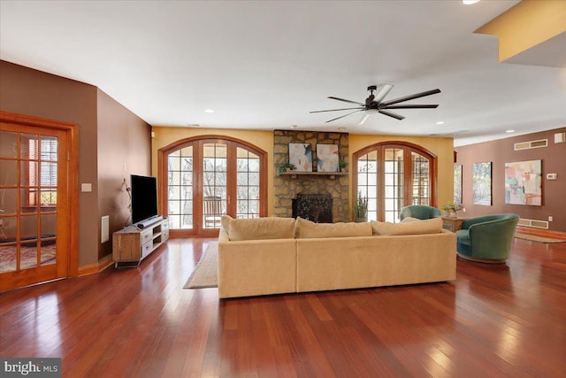 living room with ceiling fan, hardwood / wood-style floors, a stone fireplace, and french doors