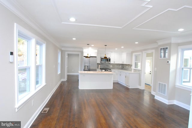 kitchen with white cabinets, appliances with stainless steel finishes, decorative light fixtures, a kitchen island, and dark hardwood / wood-style flooring