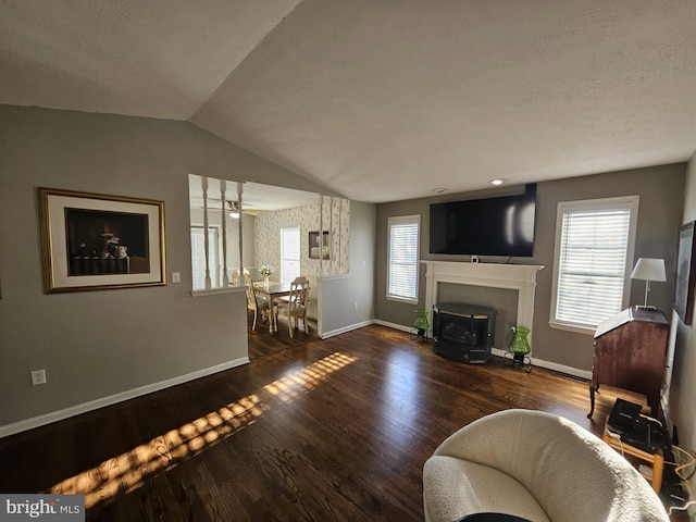 living room featuring a wood stove, dark wood-type flooring, vaulted ceiling, and a healthy amount of sunlight