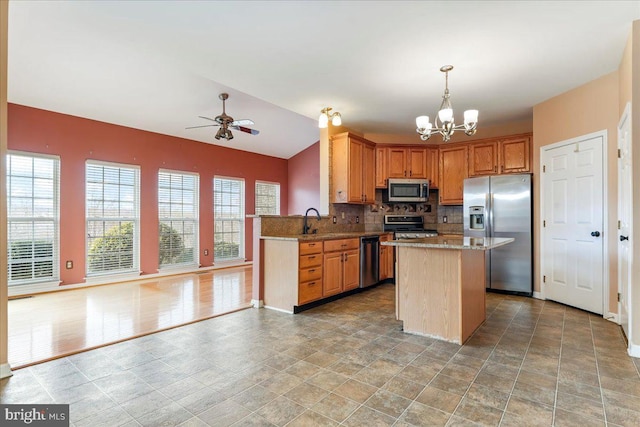 kitchen with backsplash, ceiling fan with notable chandelier, hanging light fixtures, appliances with stainless steel finishes, and a kitchen island