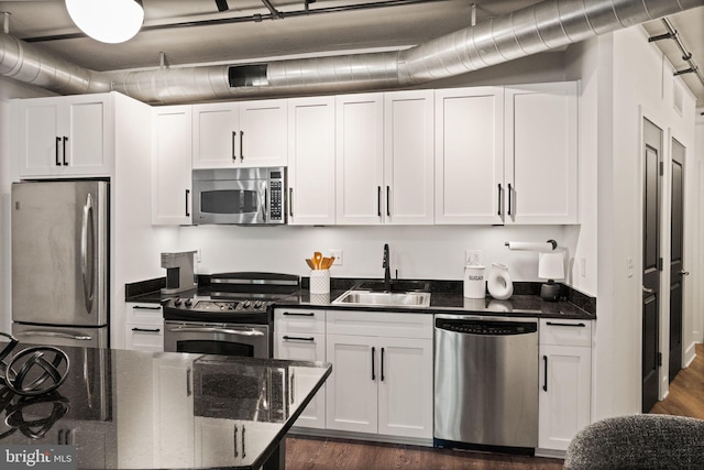 kitchen with a sink, dark stone counters, appliances with stainless steel finishes, and white cabinets