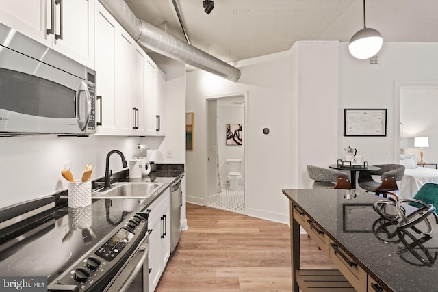kitchen featuring appliances with stainless steel finishes, a sink, light wood finished floors, dark stone counters, and white cabinetry