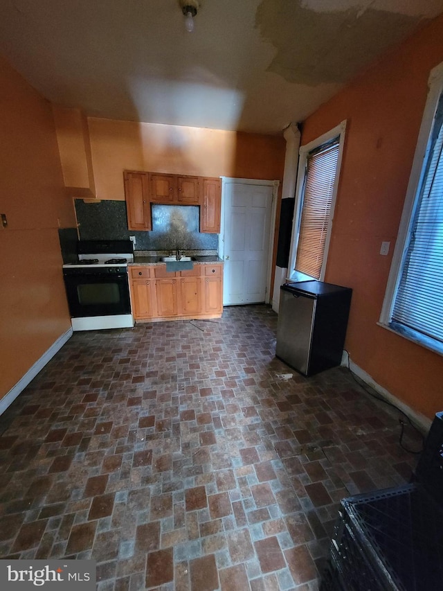 kitchen featuring refrigerator, sink, white gas range oven, and tasteful backsplash