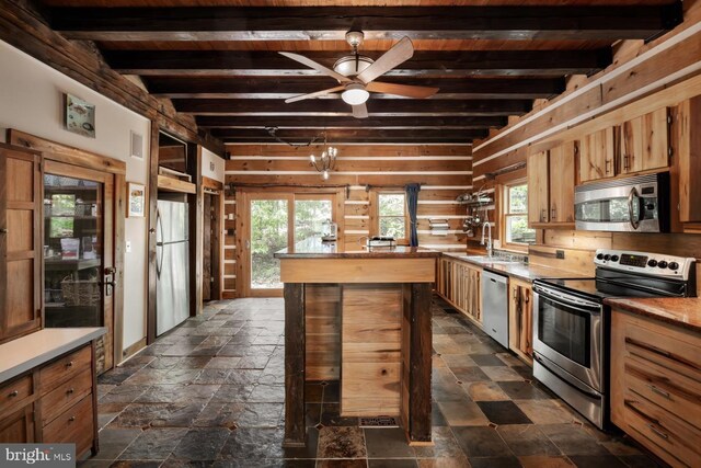 kitchen featuring stainless steel appliances, beamed ceiling, a sink, healthy amount of natural light, and stone tile floors