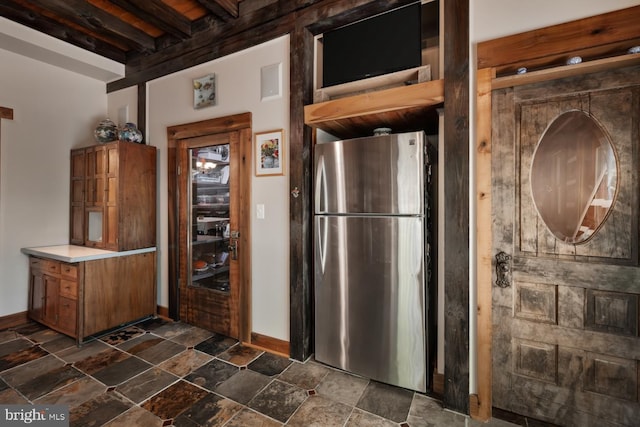 kitchen with freestanding refrigerator, brown cabinets, dark stone finish floors, baseboards, and light countertops