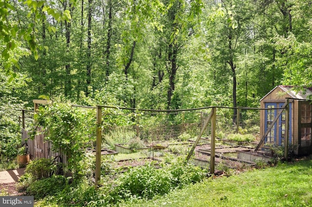 view of yard with a vegetable garden, fence, an outdoor structure, a storage unit, and a forest view