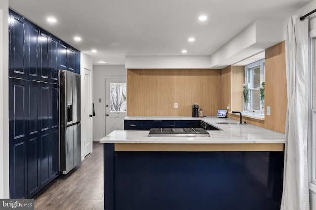 kitchen featuring appliances with stainless steel finishes, kitchen peninsula, hardwood / wood-style flooring, sink, and blue cabinets