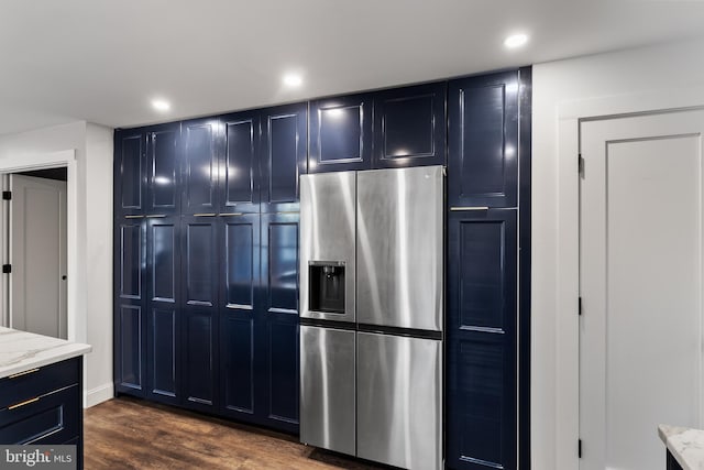 kitchen featuring stainless steel fridge, blue cabinetry, light stone countertops, and dark wood-type flooring