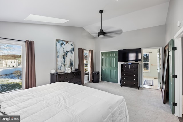 bedroom featuring ensuite bathroom, a closet, lofted ceiling with skylight, ceiling fan, and light carpet