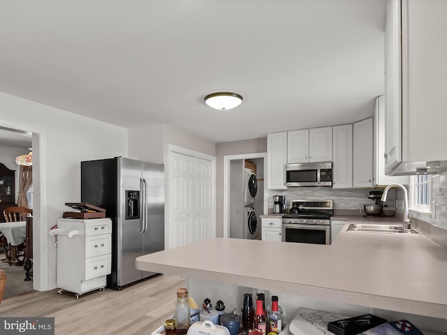 kitchen with sink, light hardwood / wood-style flooring, appliances with stainless steel finishes, stacked washing maching and dryer, and white cabinets