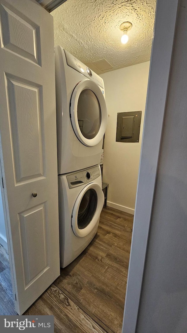 washroom featuring a textured ceiling, electric panel, dark hardwood / wood-style floors, and stacked washer and clothes dryer