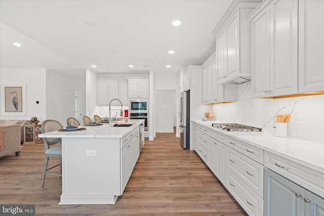 kitchen with a breakfast bar, a kitchen island with sink, light hardwood / wood-style floors, white cabinetry, and stainless steel appliances