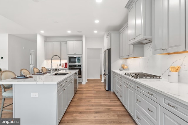 kitchen with appliances with stainless steel finishes, light wood-type flooring, backsplash, a breakfast bar, and a center island with sink