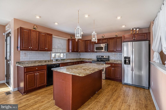 kitchen with hanging light fixtures, sink, light wood-type flooring, appliances with stainless steel finishes, and a kitchen island