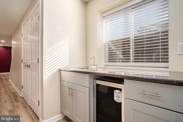 kitchen featuring sink, beverage cooler, dark stone counters, light hardwood / wood-style floors, and white cabinets