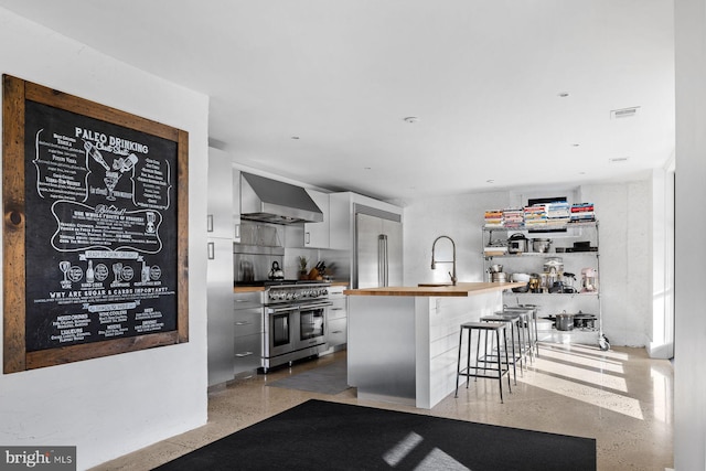 kitchen with wall chimney exhaust hood, tasteful backsplash, butcher block countertops, a breakfast bar area, and high quality appliances