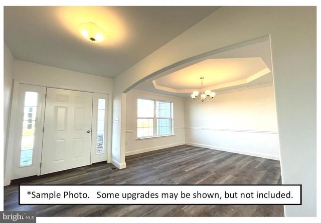 entrance foyer with a raised ceiling, dark hardwood / wood-style floors, and an inviting chandelier