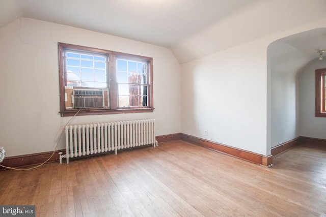 additional living space featuring cooling unit, light wood-type flooring, radiator, and vaulted ceiling