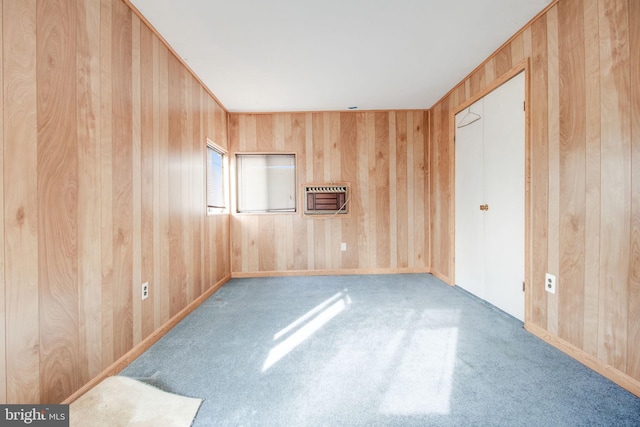 carpeted empty room featuring wood walls and heating unit