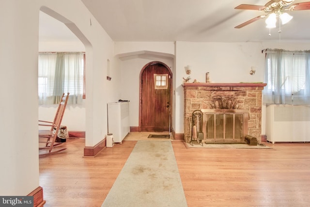 foyer entrance featuring radiator, ceiling fan, light hardwood / wood-style flooring, and a stone fireplace