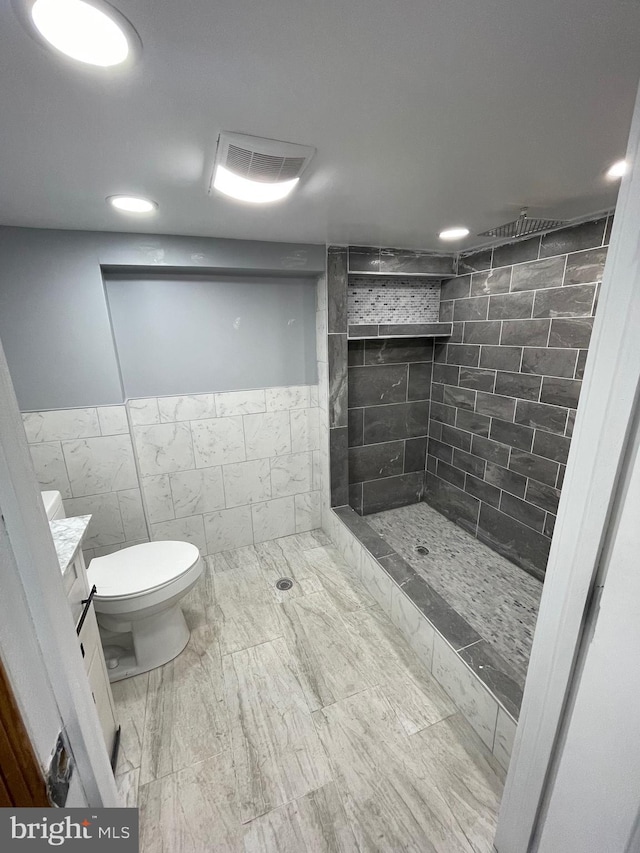 bathroom featuring a tile shower, vanity, toilet, and tile walls