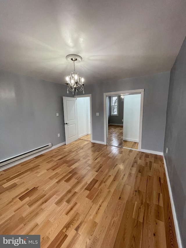 empty room with a chandelier, light hardwood / wood-style floors, and baseboard heating