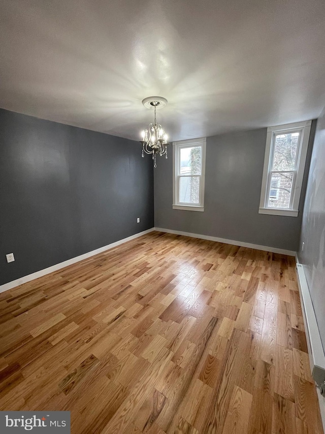 unfurnished room featuring an inviting chandelier and light hardwood / wood-style flooring