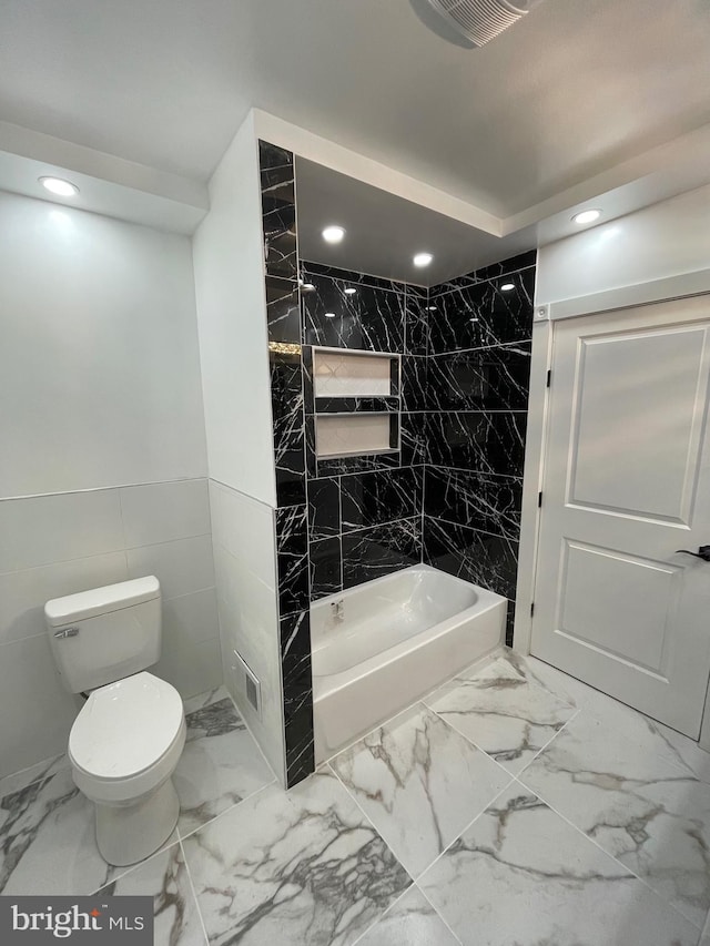 bathroom with tiled shower / bath combo, tile walls, and toilet