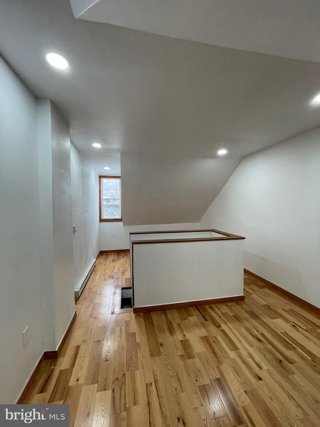 bonus room with a baseboard radiator, vaulted ceiling, and light wood-type flooring