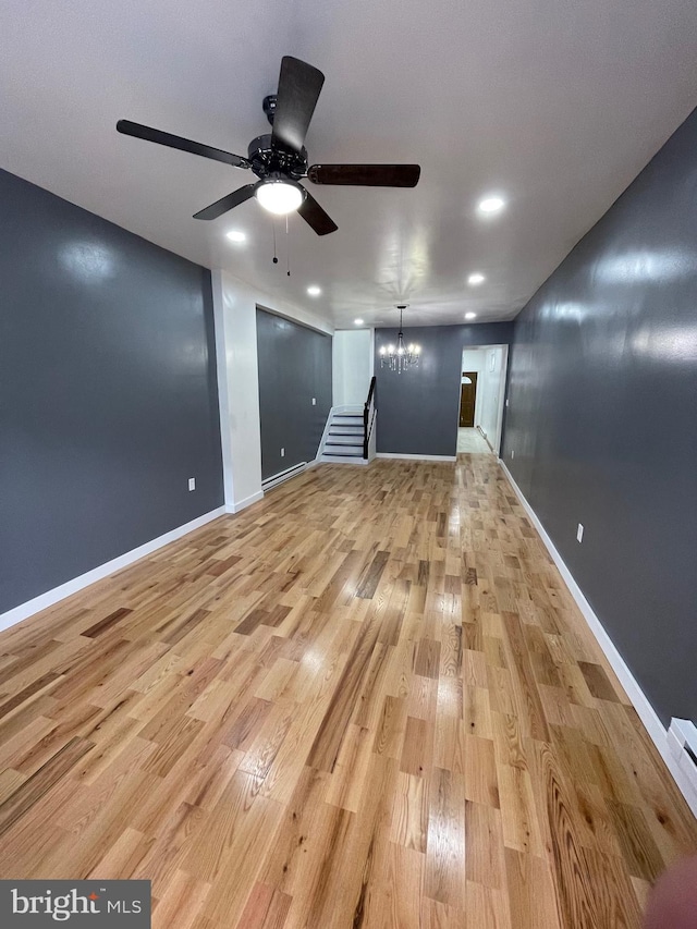 unfurnished living room with ceiling fan with notable chandelier and light hardwood / wood-style flooring