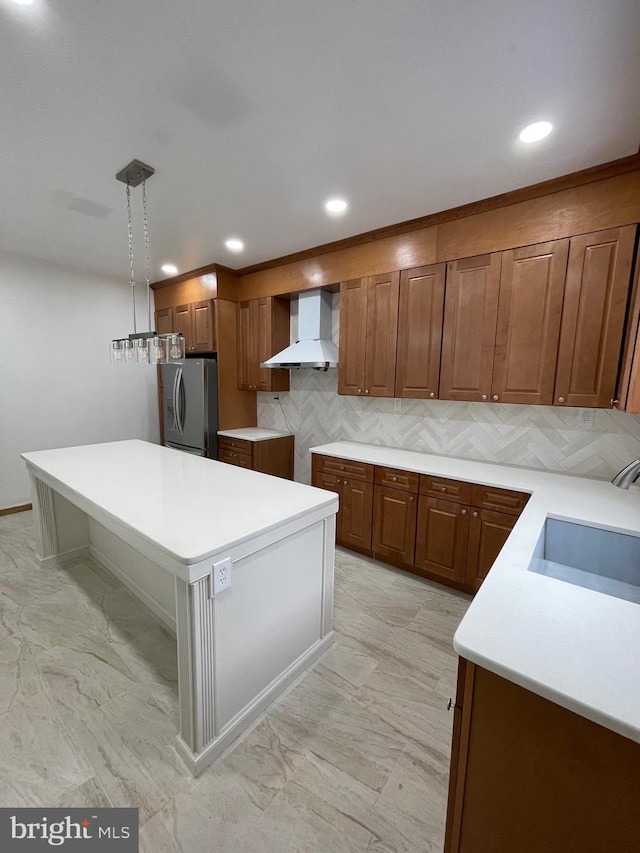 kitchen with decorative backsplash, stainless steel refrigerator with ice dispenser, sink, wall chimney range hood, and decorative light fixtures